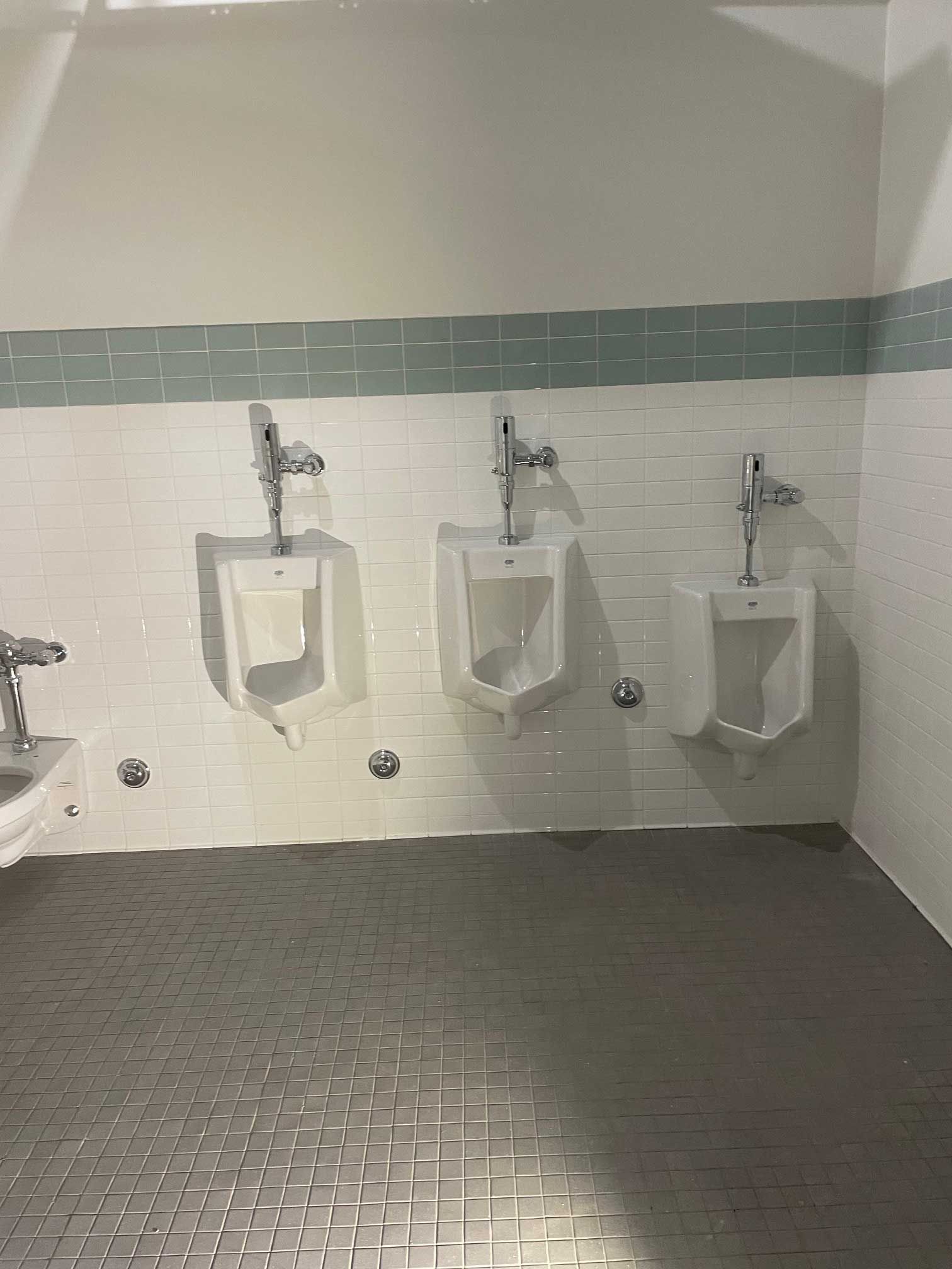 urinals mounted on a white-tiled wall in a public restroom