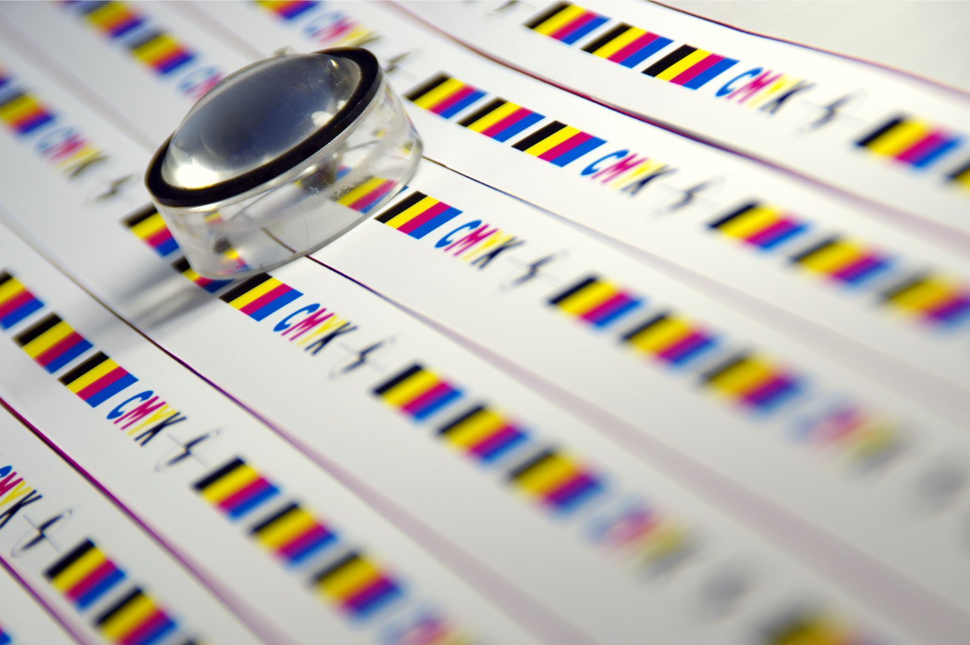 Rows of CMYK color bars on paper, with a magnifying glass resting on one.