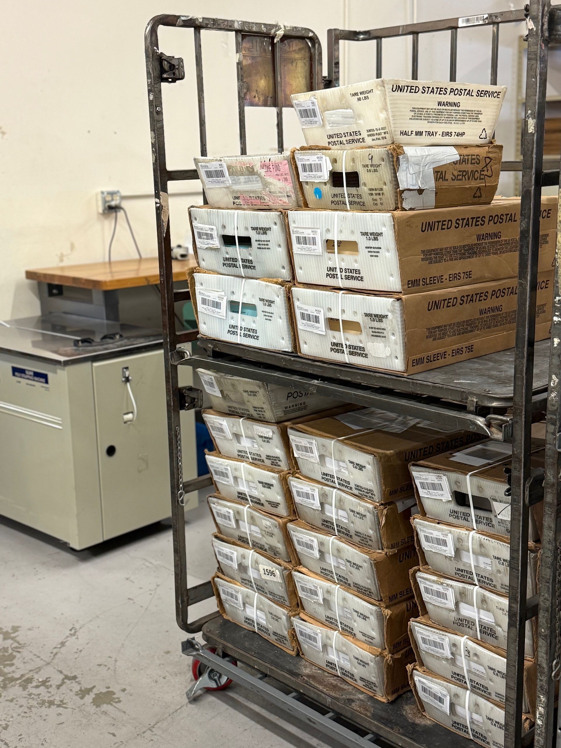 Boxes stacked on a metal cart in a laboratory. A water bath and counter are visible.
