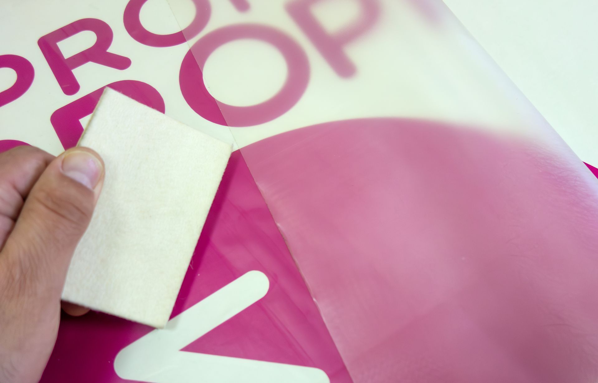 Hand using a squeegee to apply a pink decal, peeling away the clear backing.