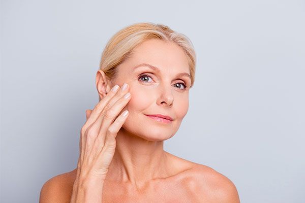 A woman is touching her face with her hand and smiling.
