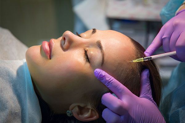 A woman is getting a botox injection in her forehead.