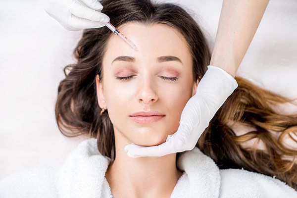 A woman is getting a botox injection in her forehead.