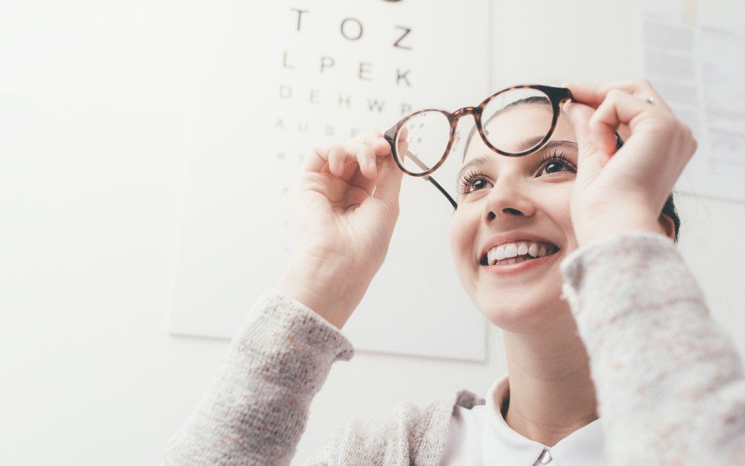 A woman is trying on glasses in front of an eye chart.