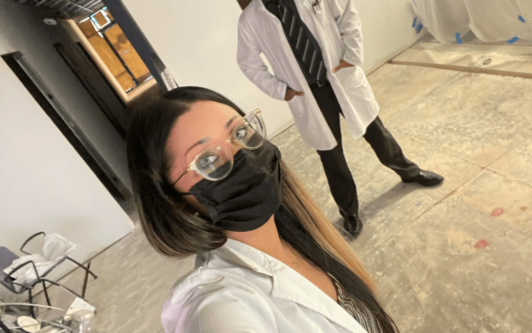 A woman wearing a mask and glasses is standing next to a man in a lab coat.