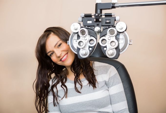 A woman is smiling while sitting in an eye exam chair.