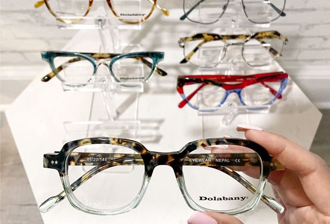 A person is holding a pair of glasses in front of a display of glasses.