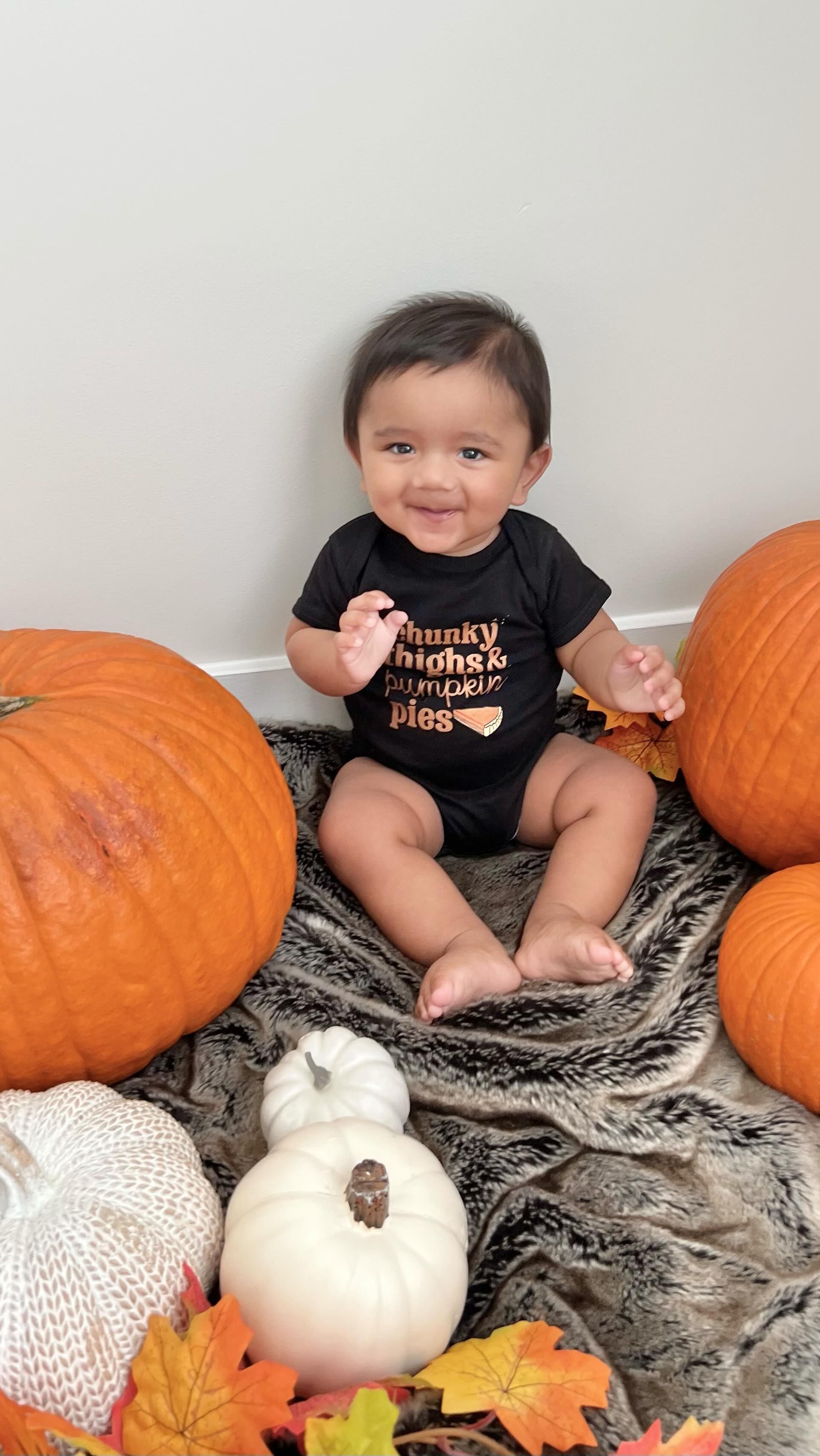 A baby is sitting on the floor surrounded by pumpkins and leaves.
