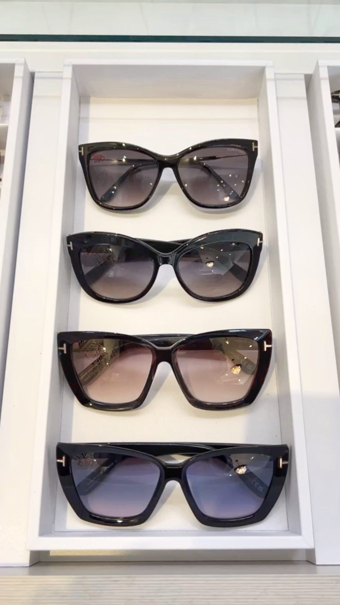 Four pairs of sunglasses are lined up on a white shelf.