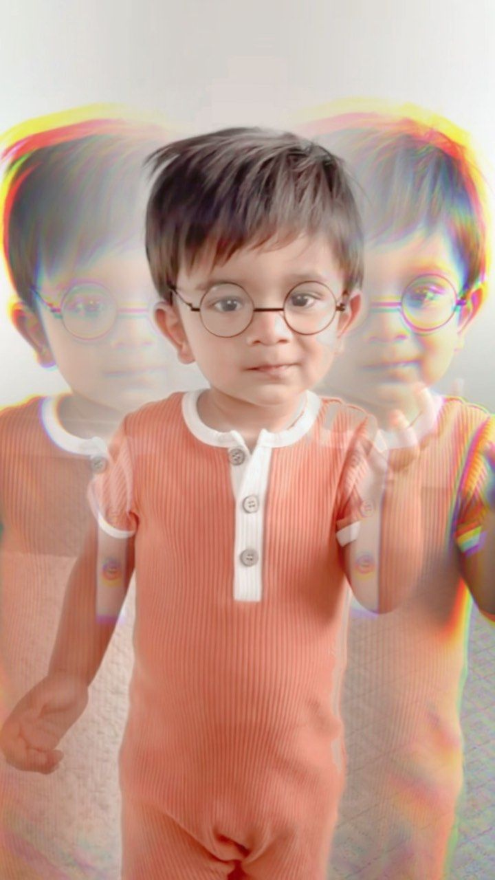 A little boy wearing glasses is standing in front of a mirror.