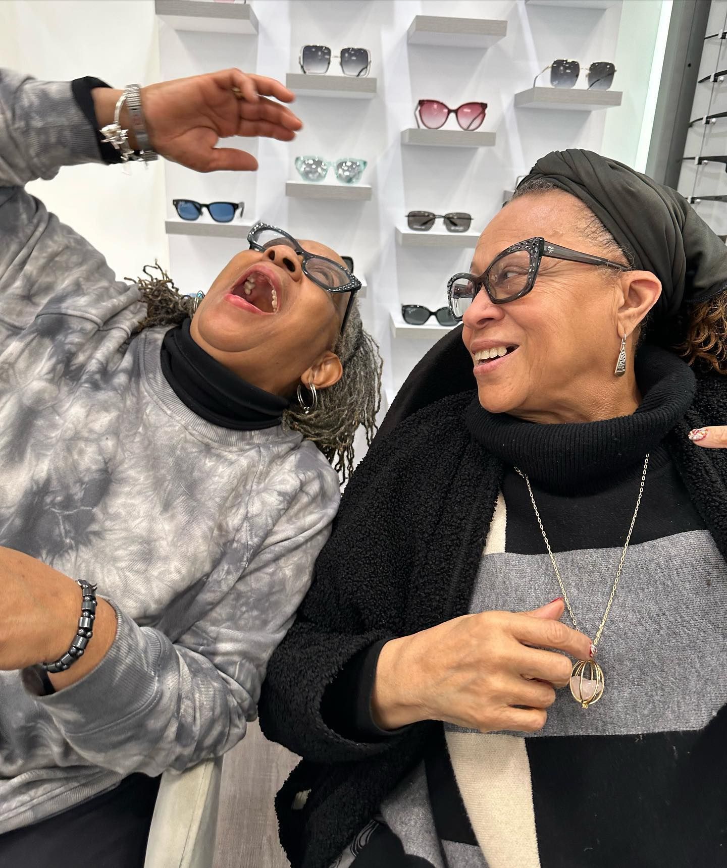 Two women wearing glasses are sitting next to each other and laughing.