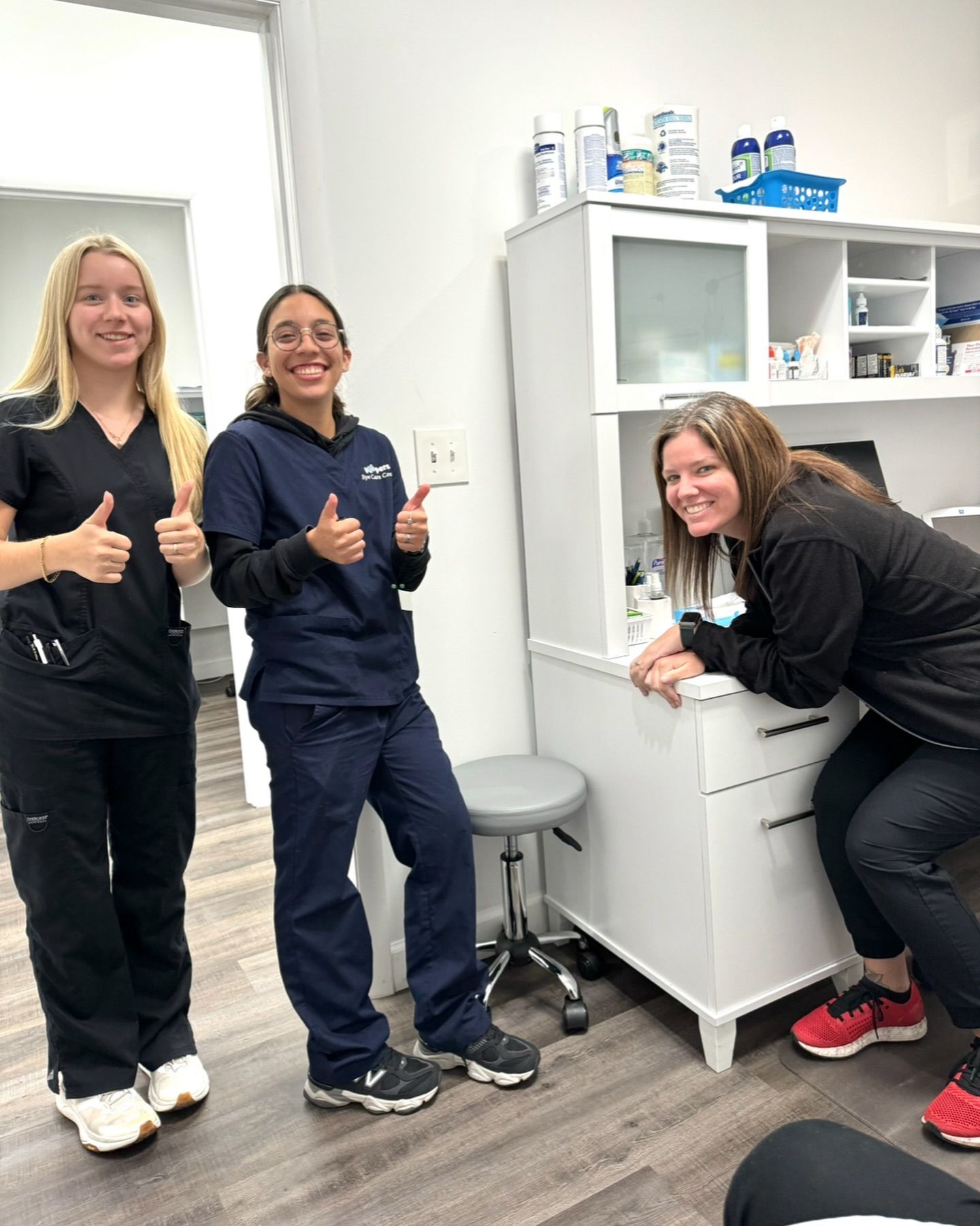 Three nurses are giving a thumbs up in a dental office.