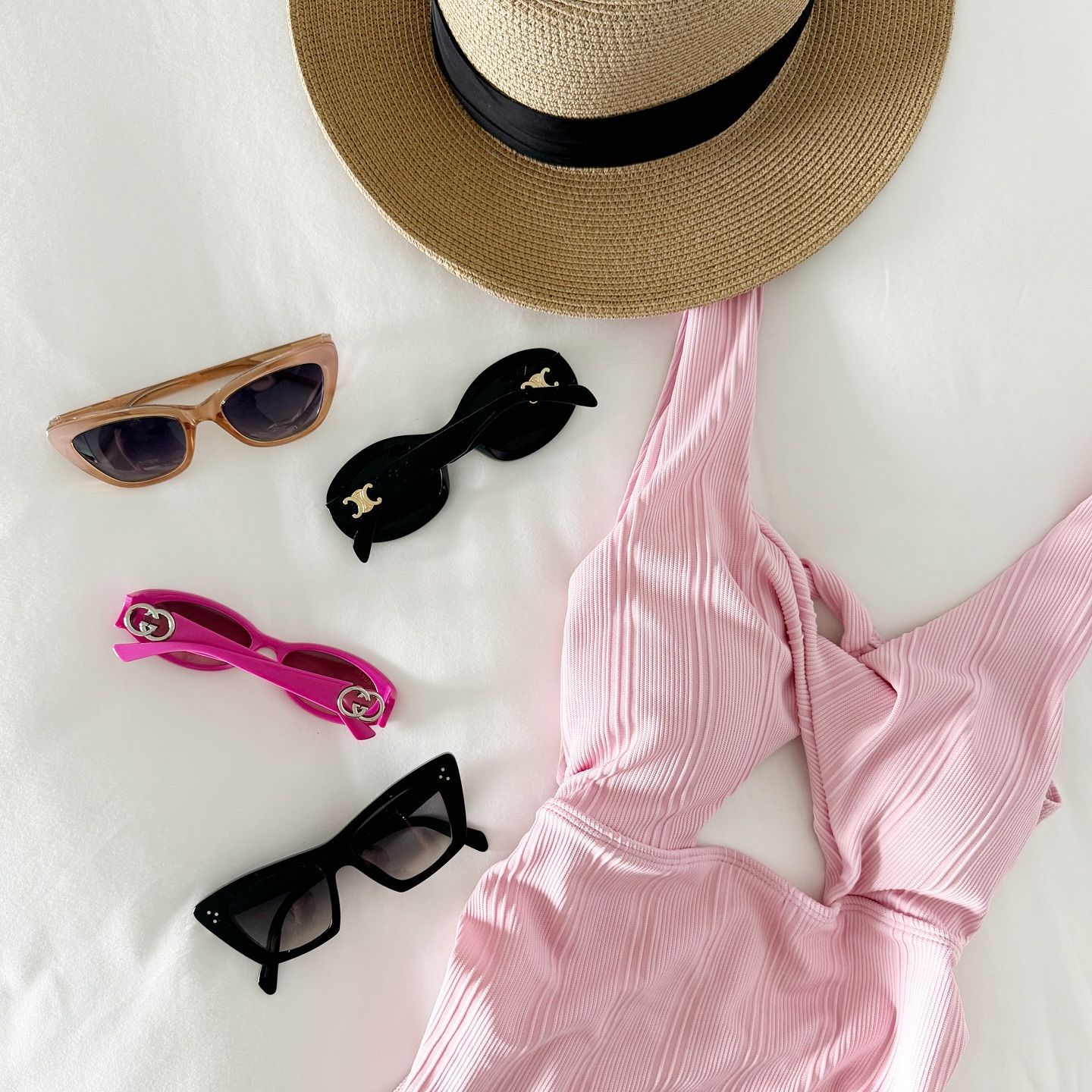 A hat , sunglasses , and a pink swimsuit are on a bed.