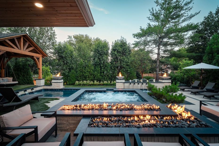 Luxury backyard pool with blue-tiled edges, waterfalls, fire features, and stone patios, surrounded by grass and landscaping.
