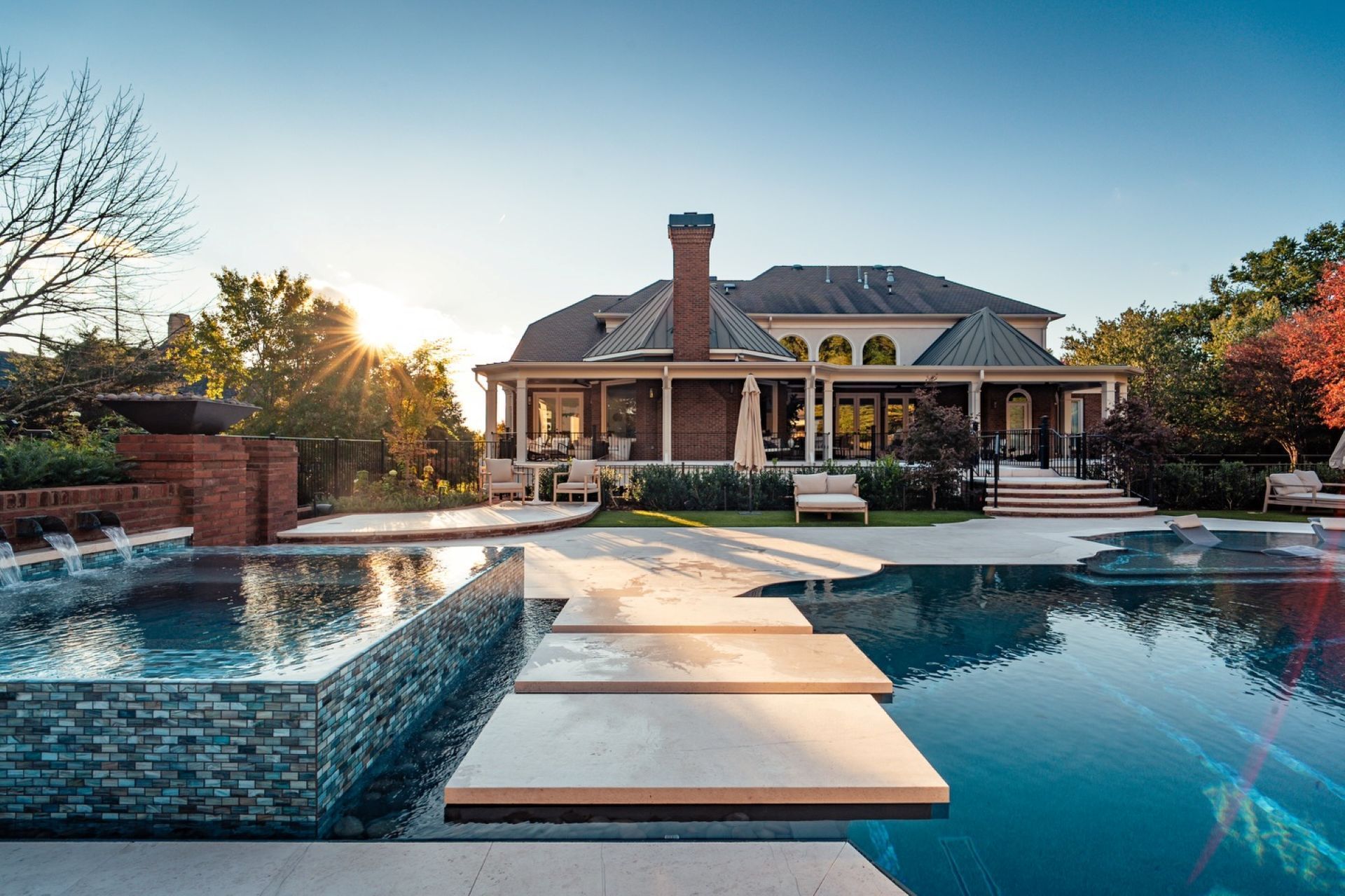 Luxury backyard pool with blue-tiled edges, waterfalls, fire features, and stone patios, surrounded by grass and landscaping.