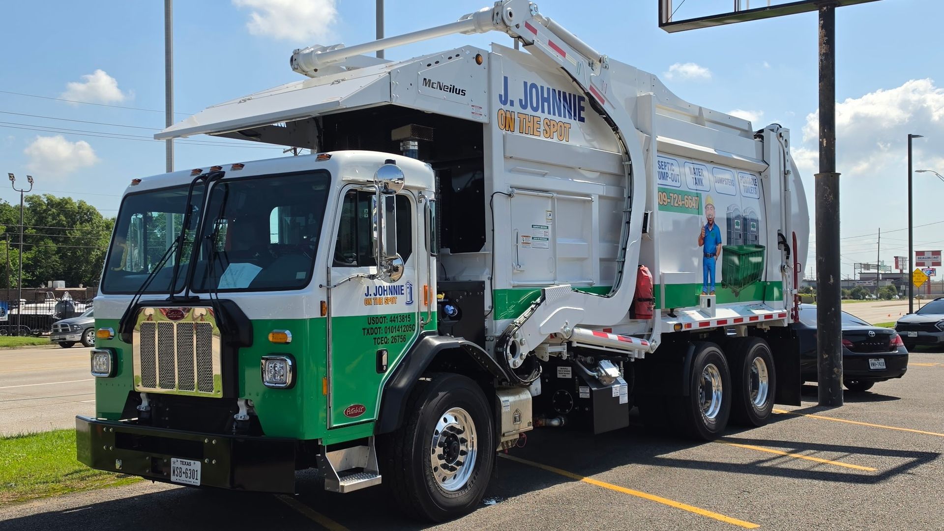 Green and white garbage truck parked in a lot under a bright blue sky