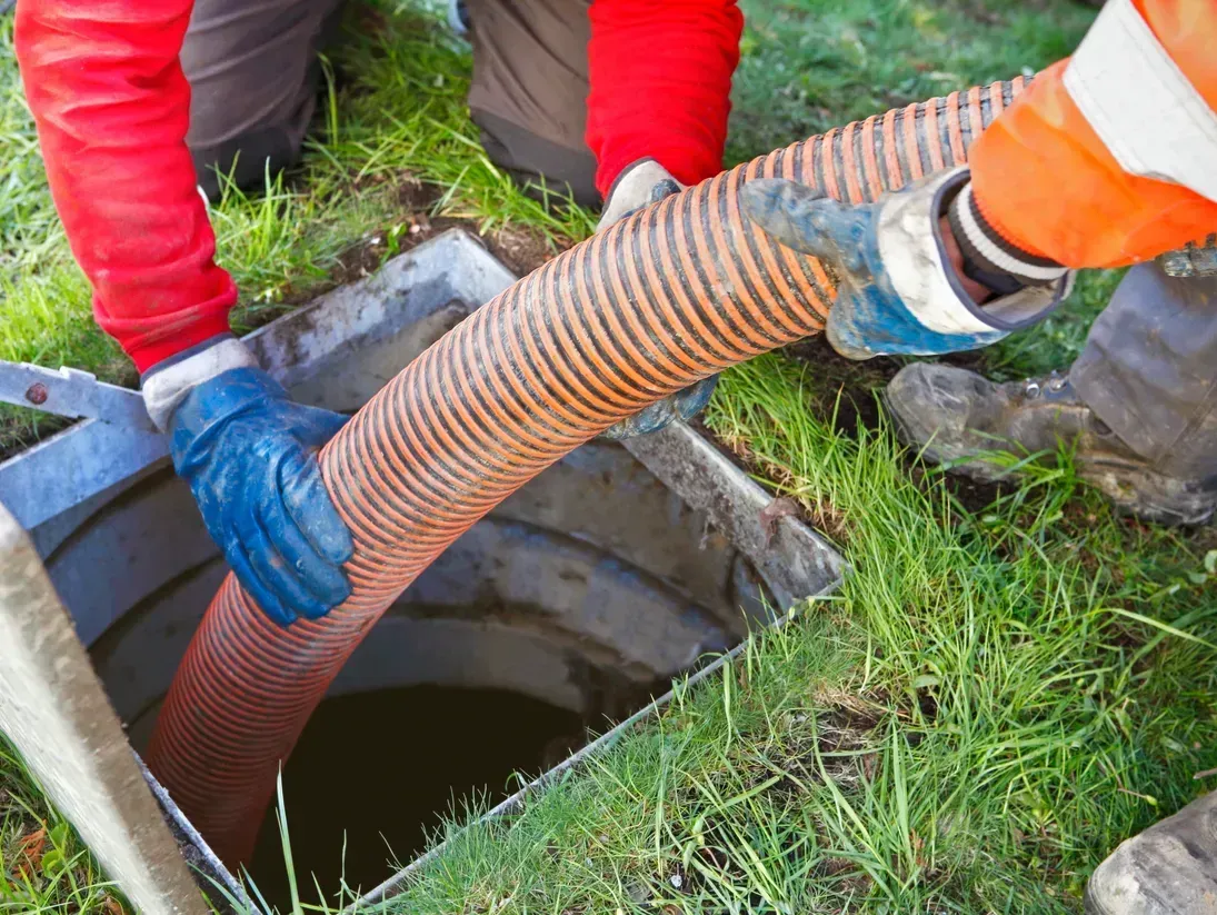 Workers in gloves removing a hose from a manhole in wet grass