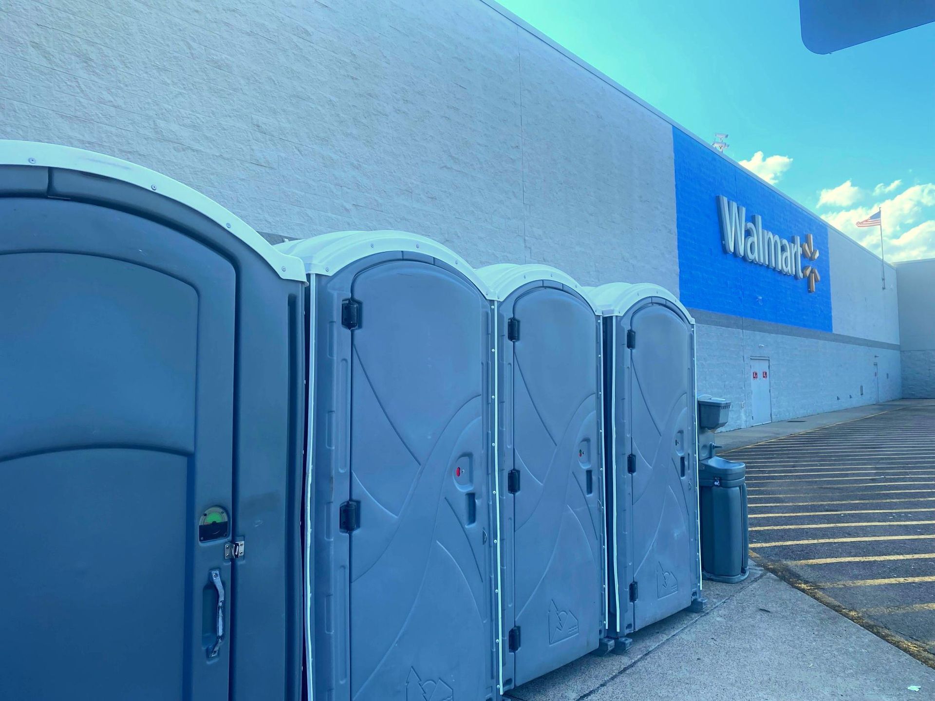 Row of gray portable toilets beside a Walmart building under a blue sky.