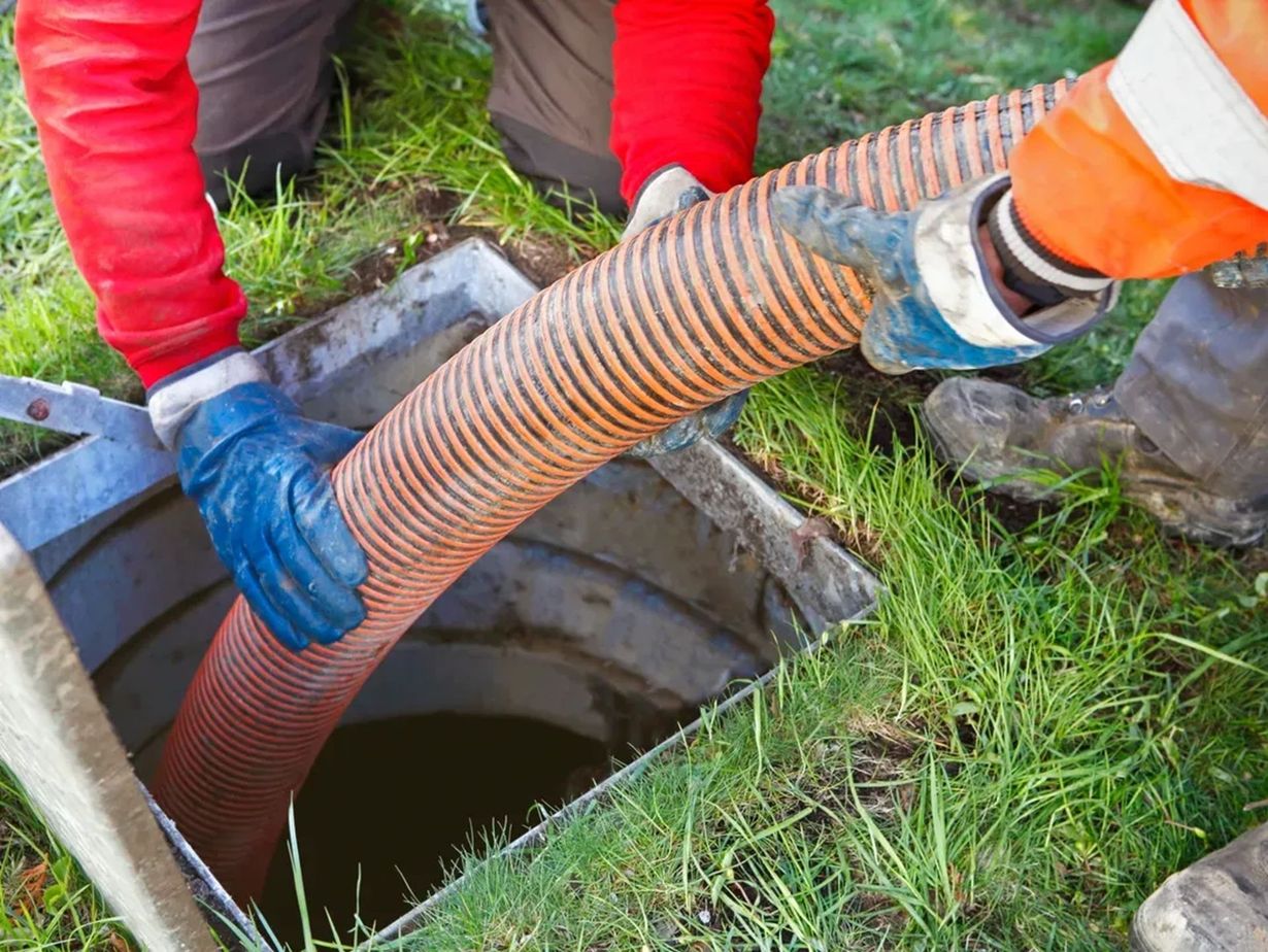 Workers lowering an orange hose into a manhole in a grassy area