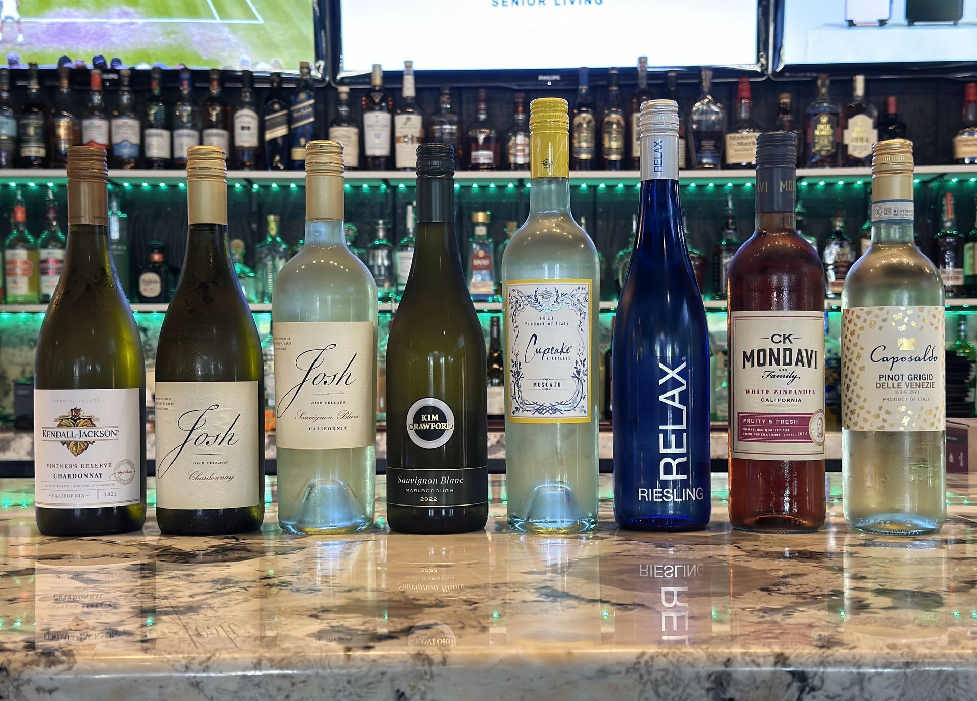 A row of bottles of wine are lined up on a bar counter