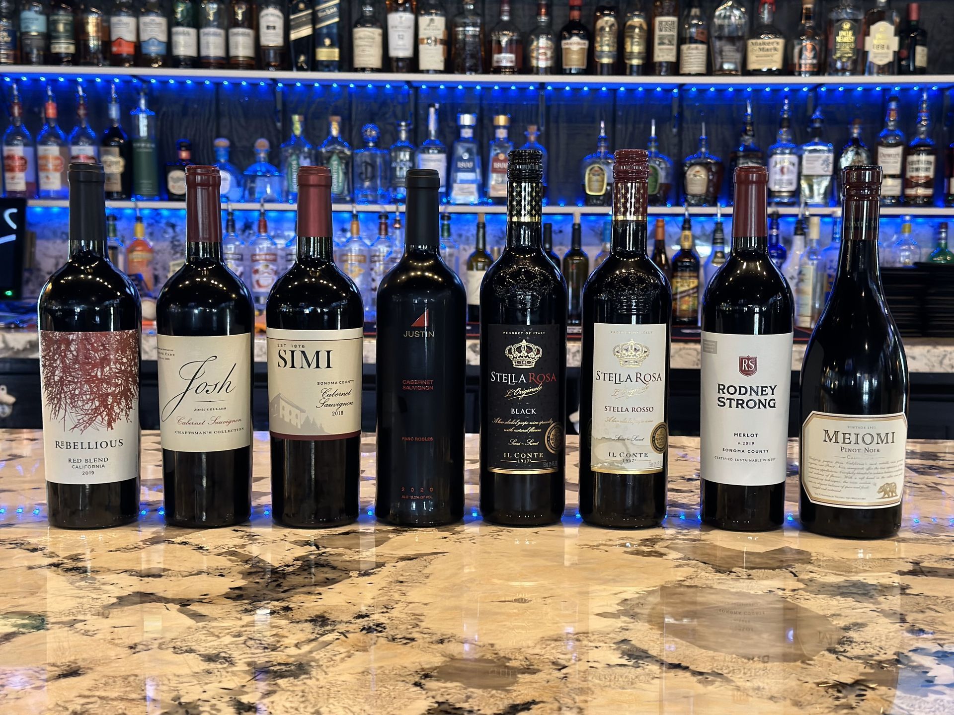 A row of wine bottles are lined up on a counter in front of a bar