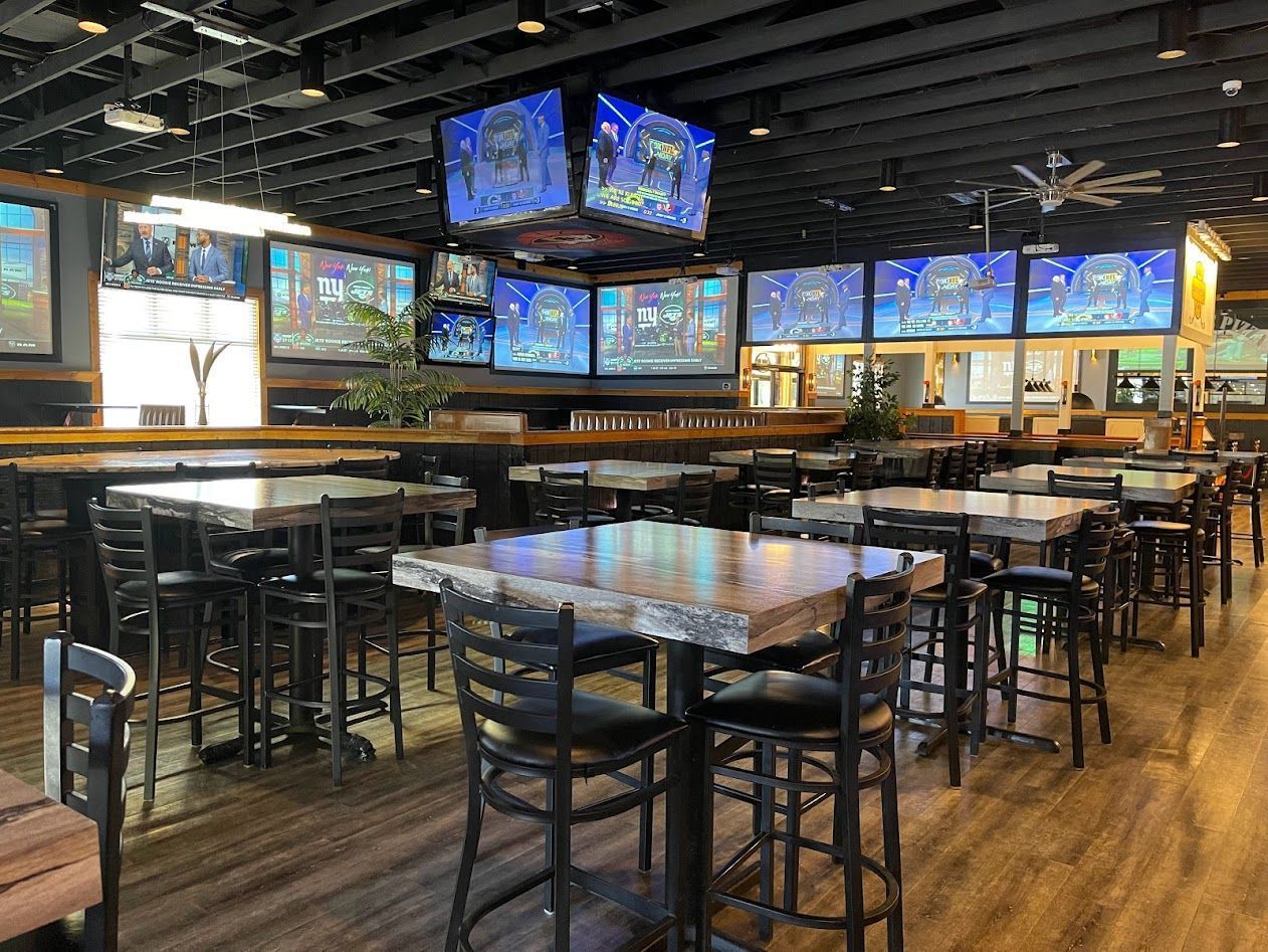 A restaurant filled with tables and chairs and televisions on the ceiling.