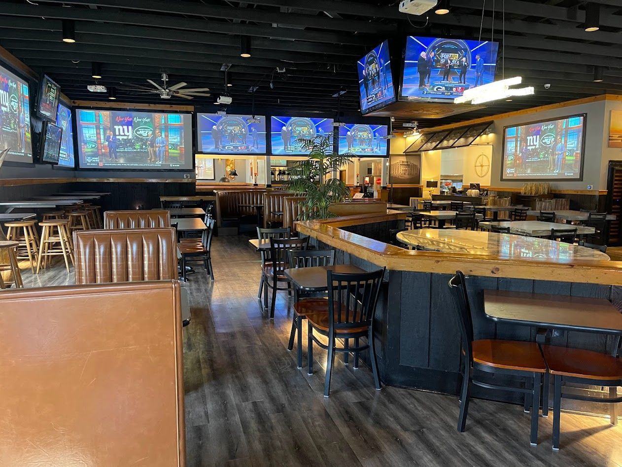 A restaurant with a lot of televisions on the ceiling and tables and chairs.
