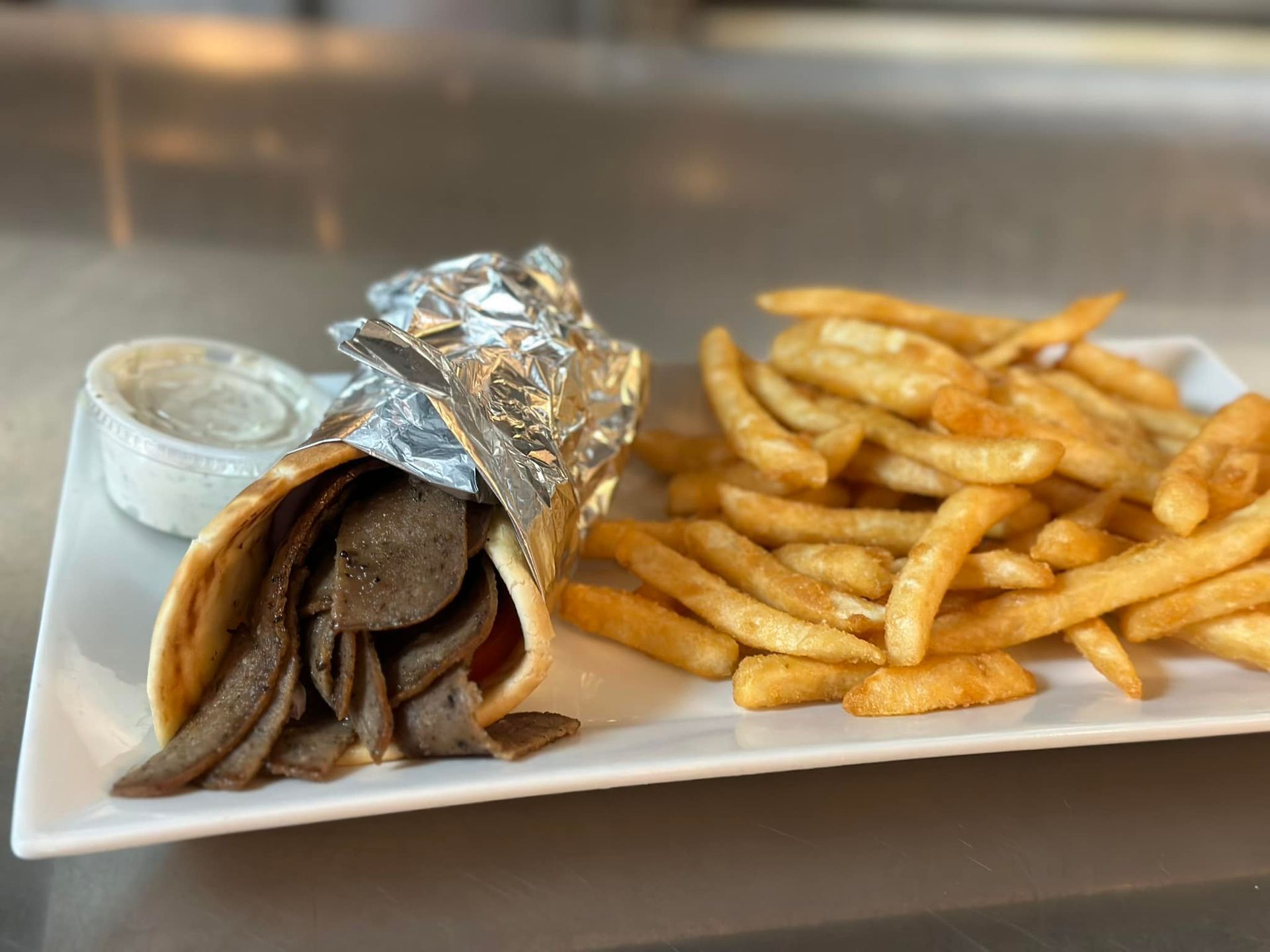 A gyro sandwich and french fries on a white plate.