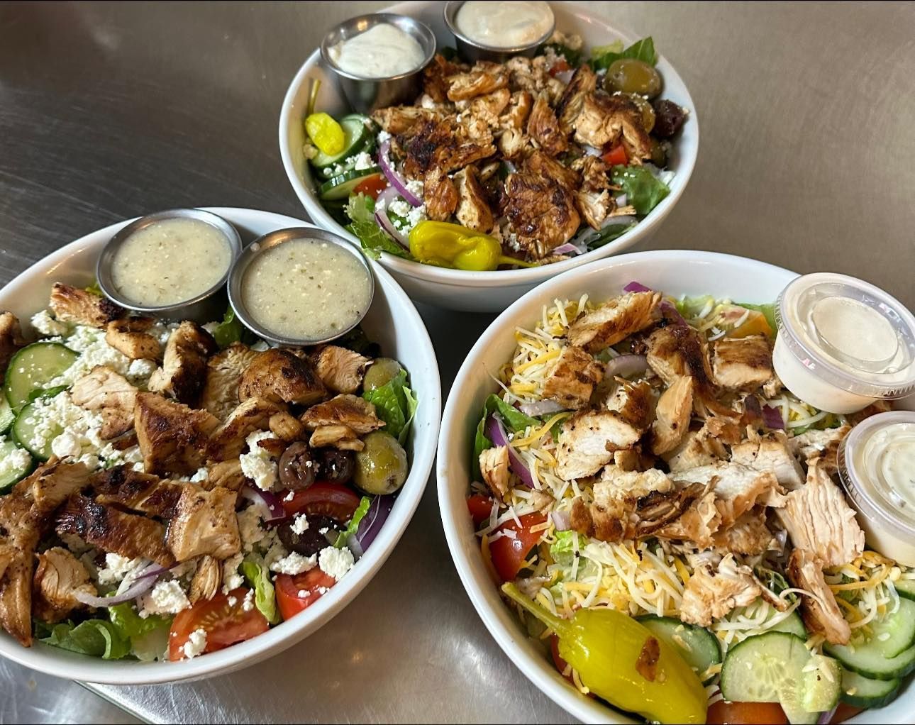 Three bowls of salad are sitting on a table.