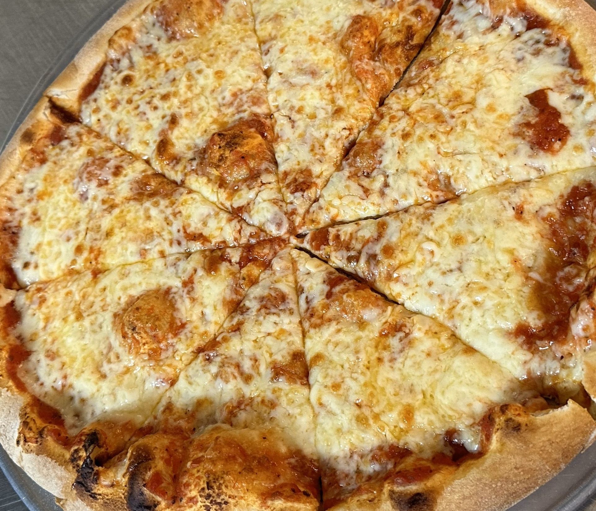 A pizza with tomato sauce and cheese is cut into slices on a plate.