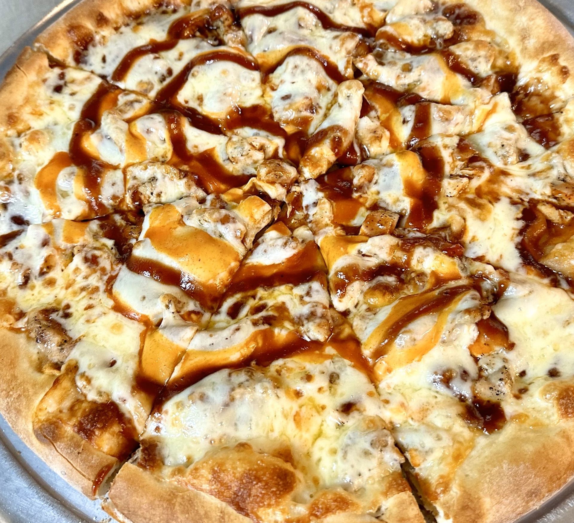 A pizza with chicken, cheese and barbecue sauce on a pan.