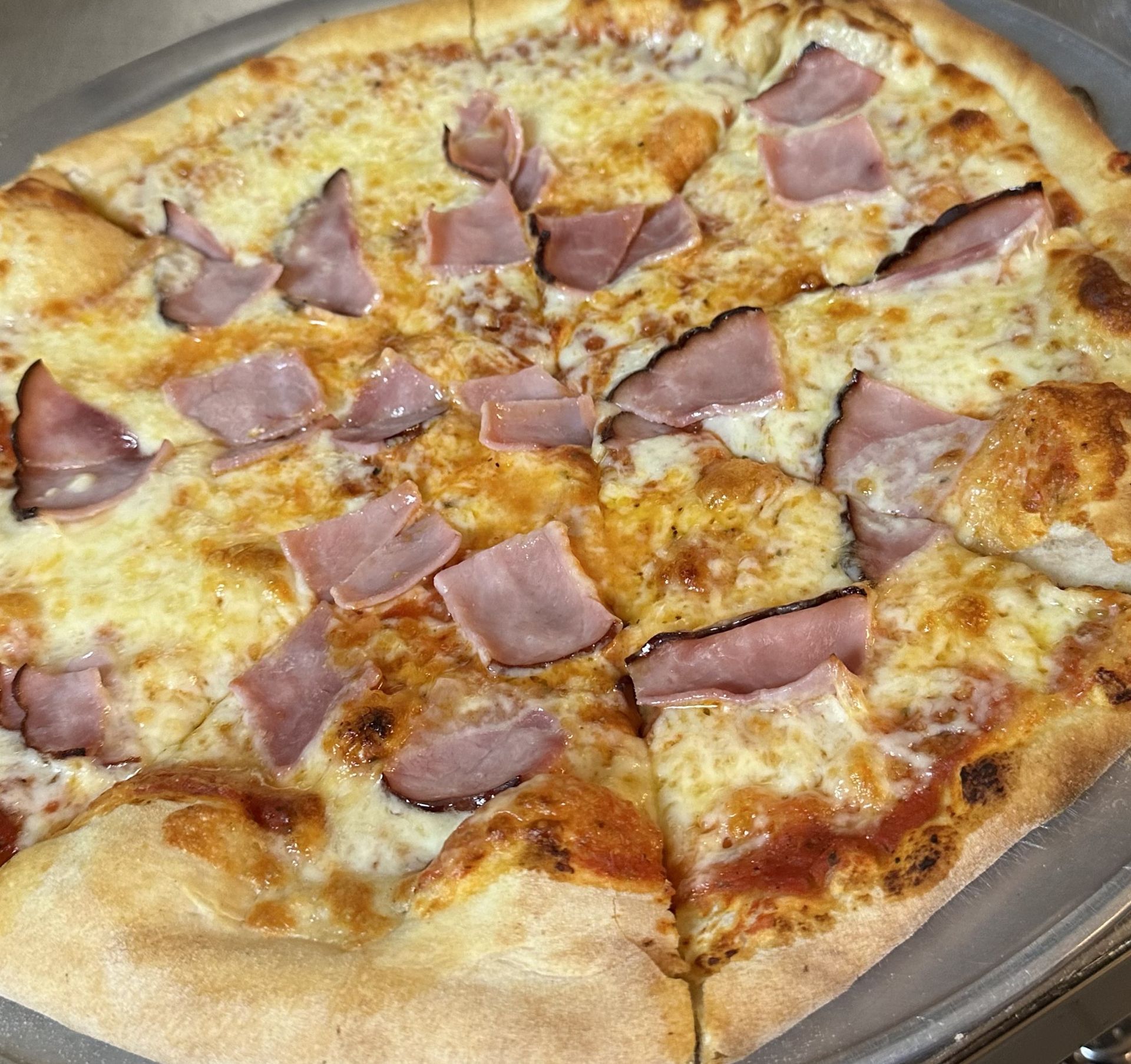 A pizza with ham and cheese on it is on a plate.