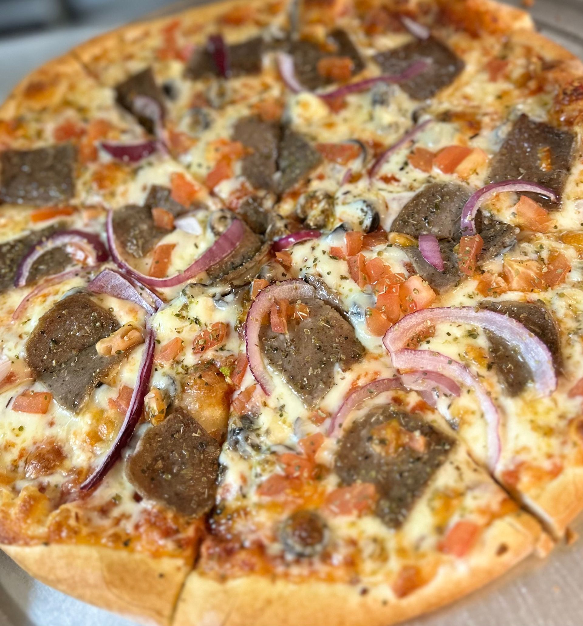 A pizza with meatballs , onions , tomatoes and cheese is sitting on a table.