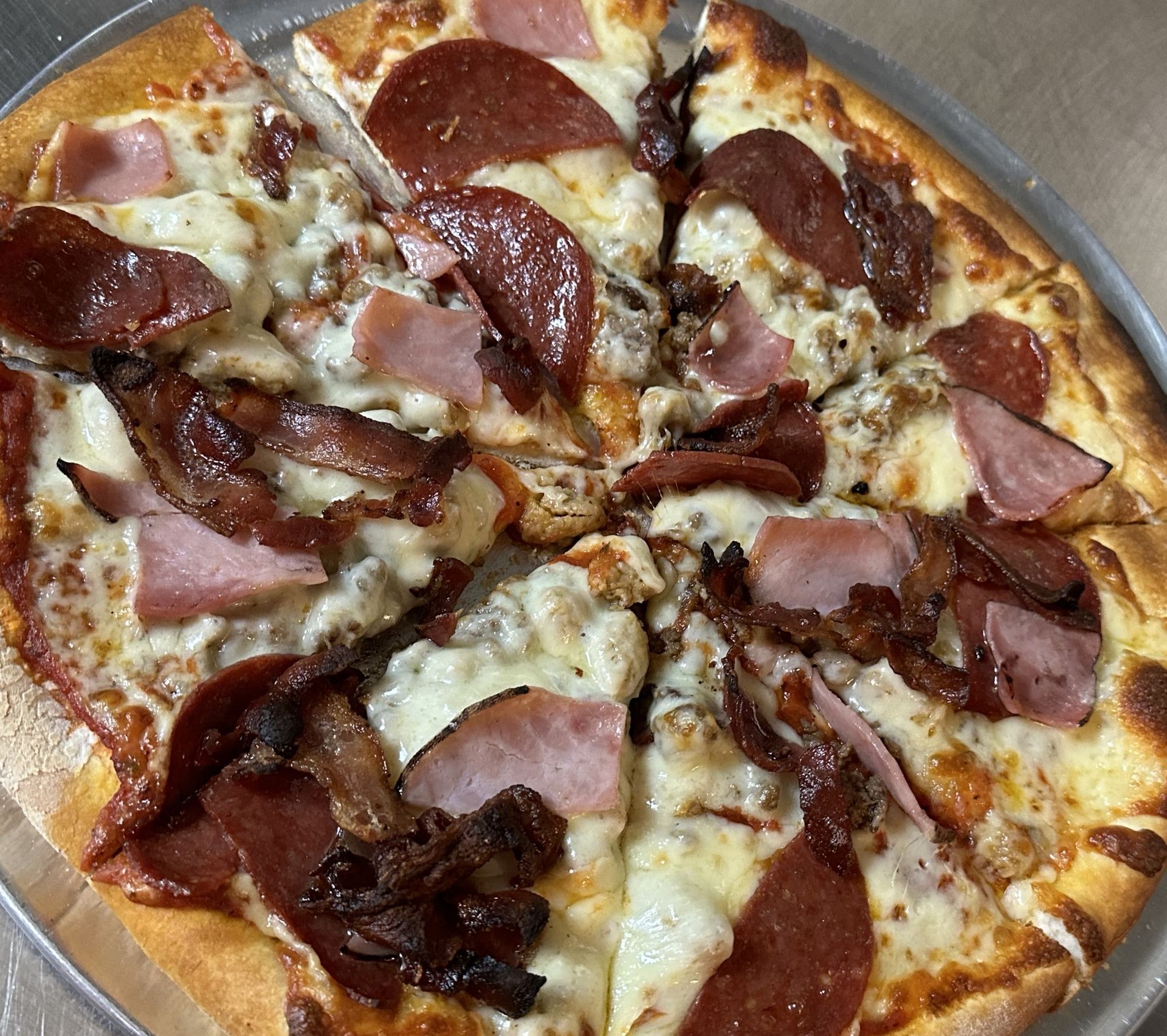 A pizza with pepperoni , ham , mushrooms and cheese on a pan.