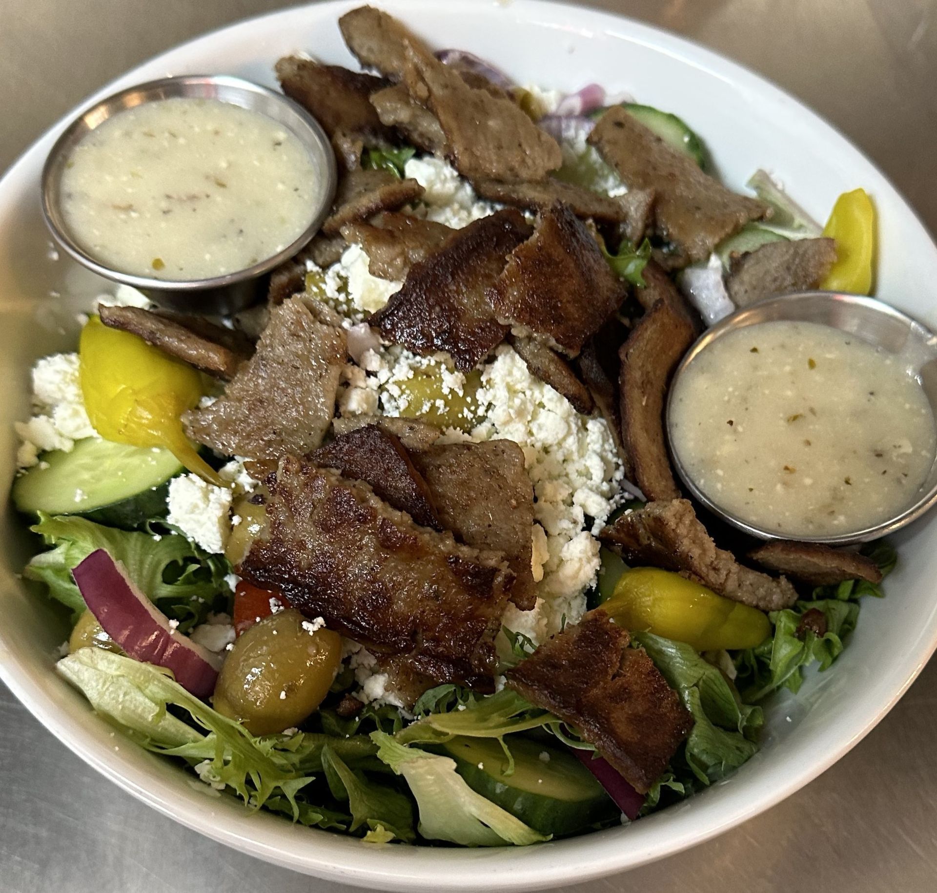 A salad with meat and vegetables in a bowl with two dipping sauces