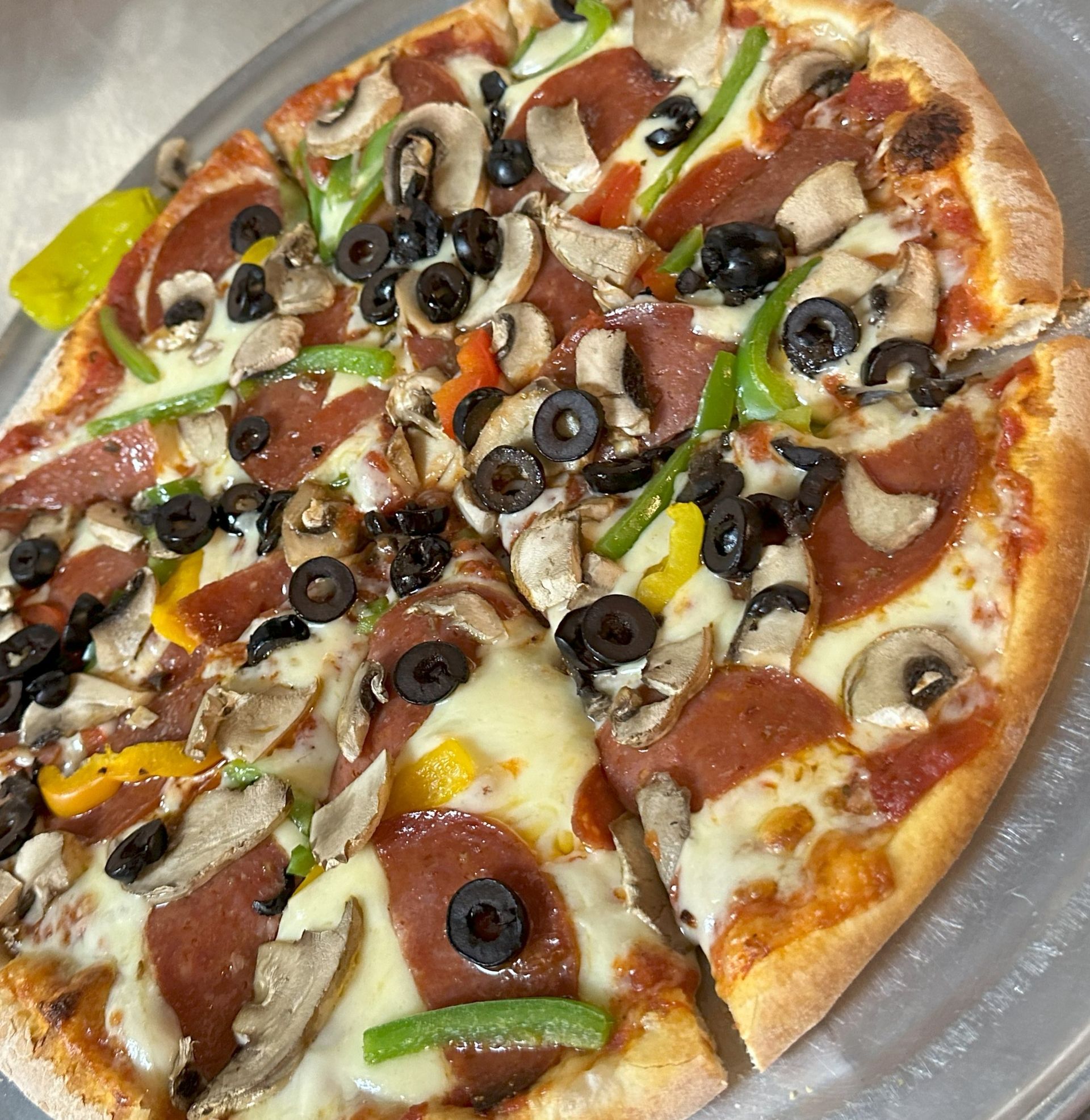 A pizza with pepperoni , mushrooms , olives and cheese is on a plate.