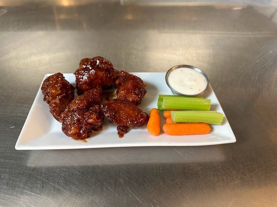 A white plate topped with chicken wings , carrots , celery and ranch dressing.
