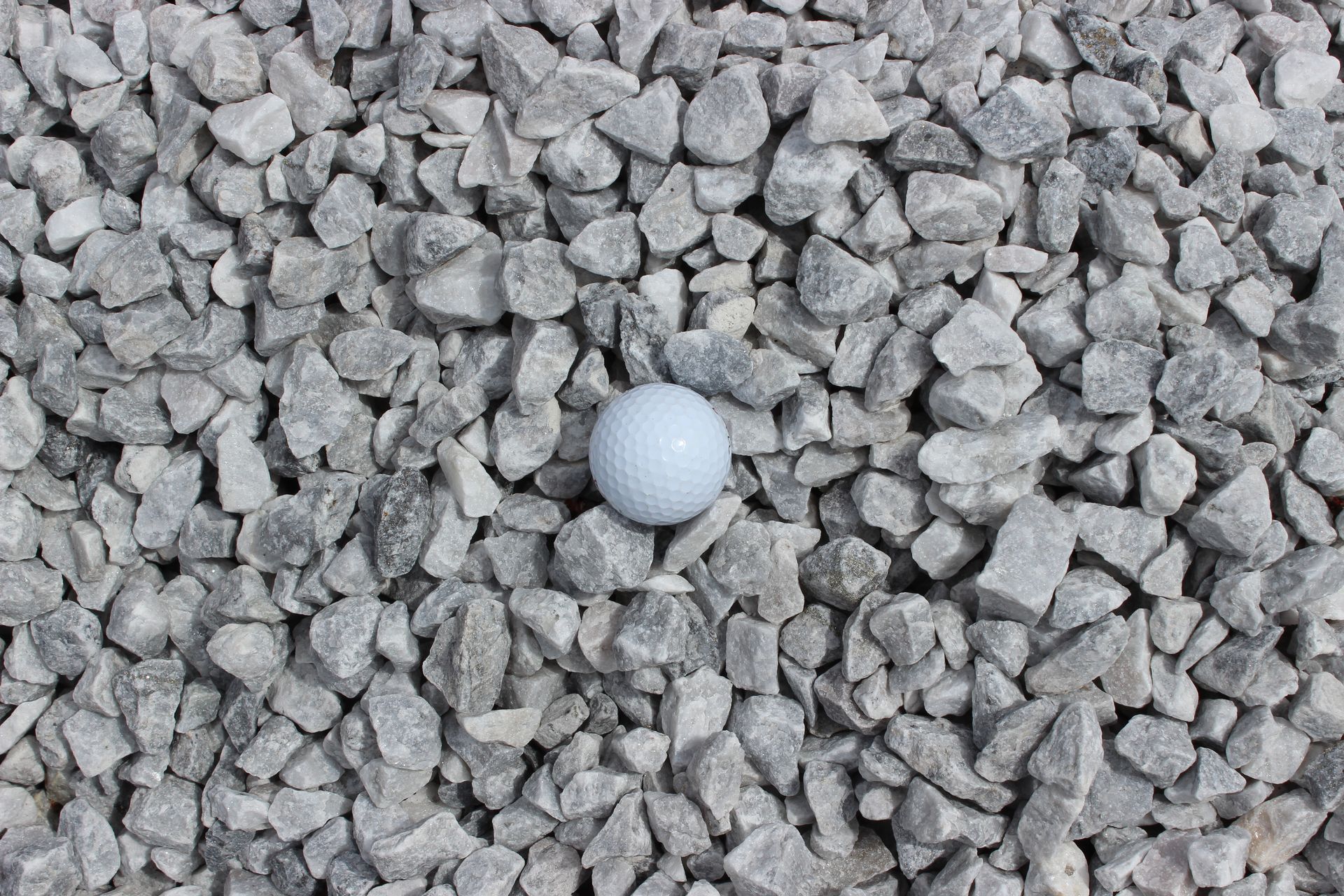 Gray gravel surrounding a white golf ball.