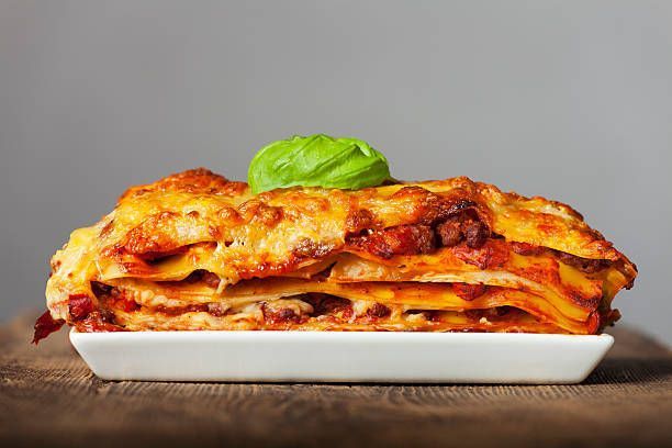A slice of lasagna is on a white plate on a wooden table