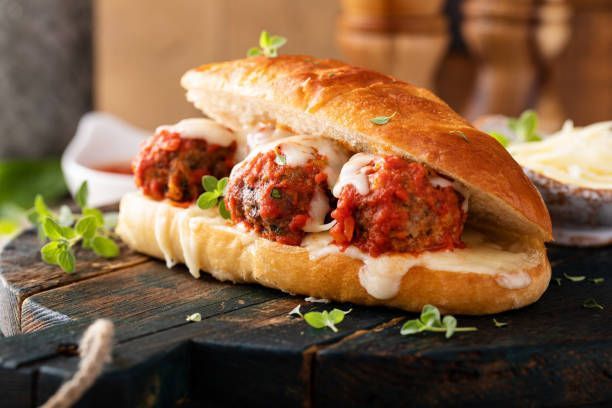 A sandwich with meatballs and cheese on a bun on a wooden table