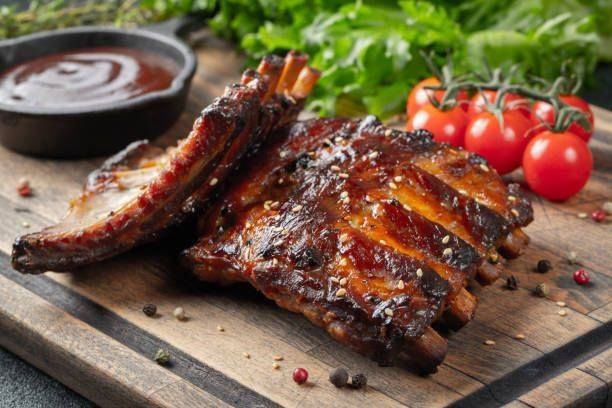 Grilled pork ribs on a wooden cutting board with tomatoes and barbecue sauce