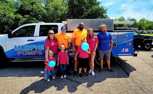 Group posing with balloons beside a blue Murphys van and trailer in a sunny parking lot