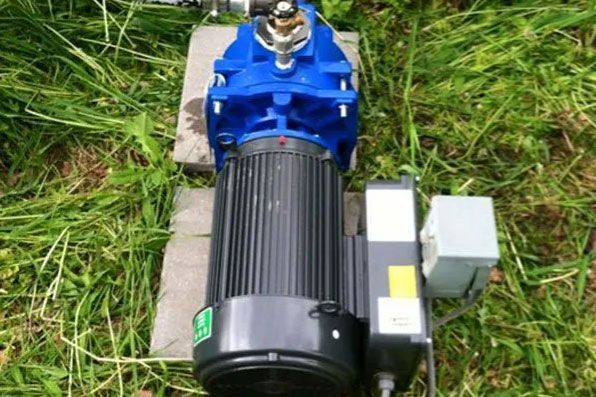 Blue and black electric motor with gearbox and control box mounted outdoors on grass and concrete block.