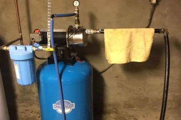 Blue water softener unit with gauges and a yellow towel hanging on a pipe in a basement.