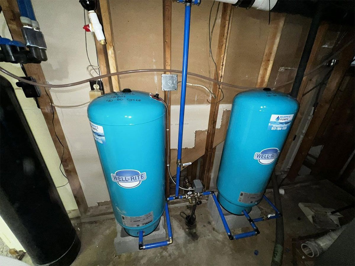 Two blue water pressure tanks in a basement utility area with exposed pipes and wooden framing