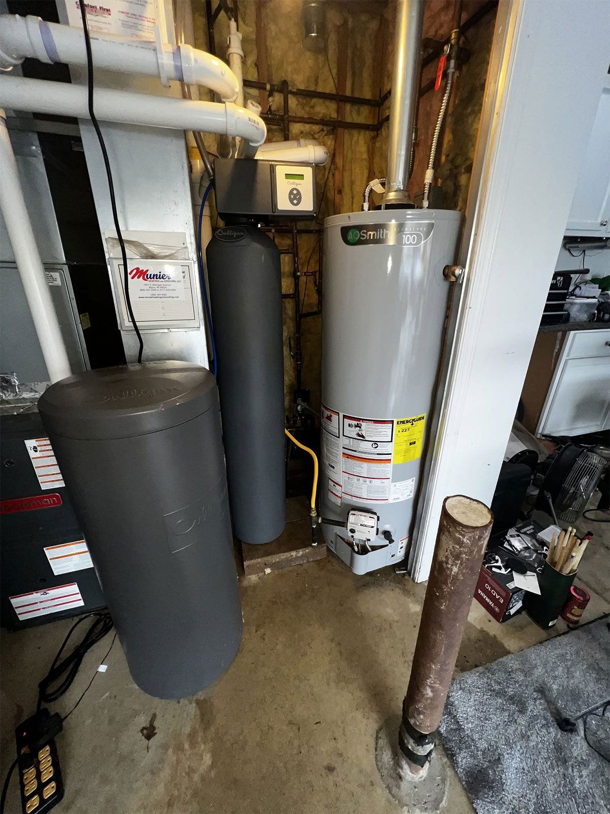 Utility room with water heater, black tanks, and exposed pipes in a basement.