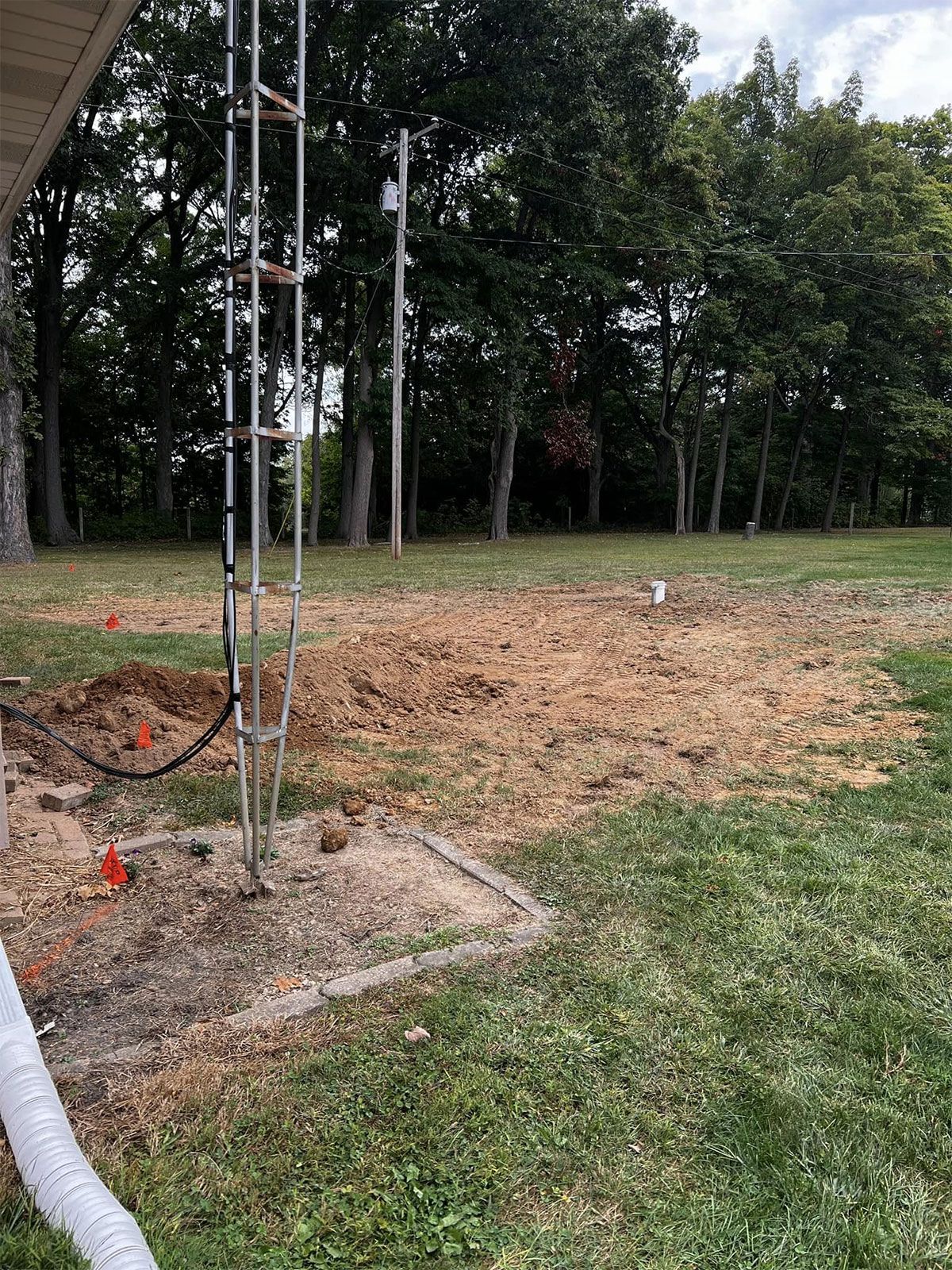 Grassy field with a metal tower base and a cleared dirt area bordered by trees.