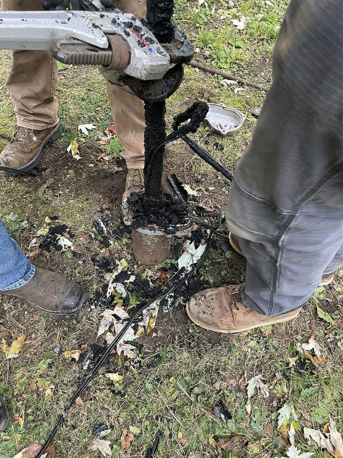 Workers using a pump to remove black sludge from a small hole in the ground outdoors
