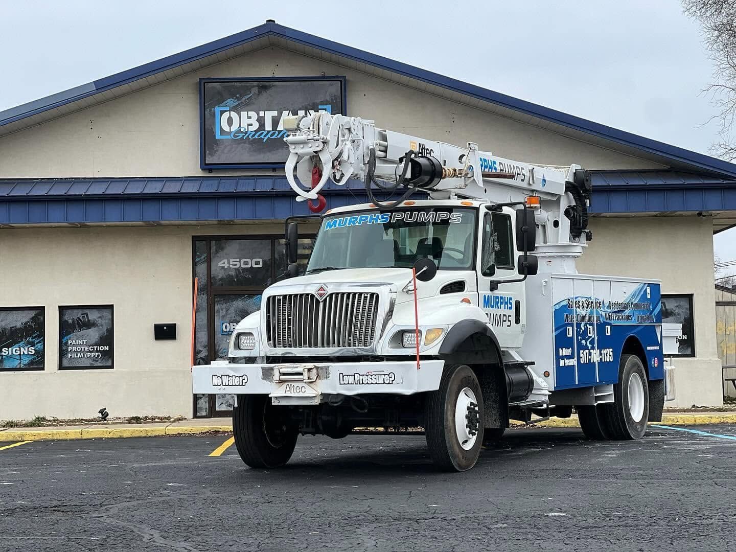 White utility truck with equipment parked outside a building on a rainy day