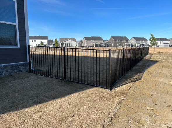 a black fence surrounds a dirt field in front of a house